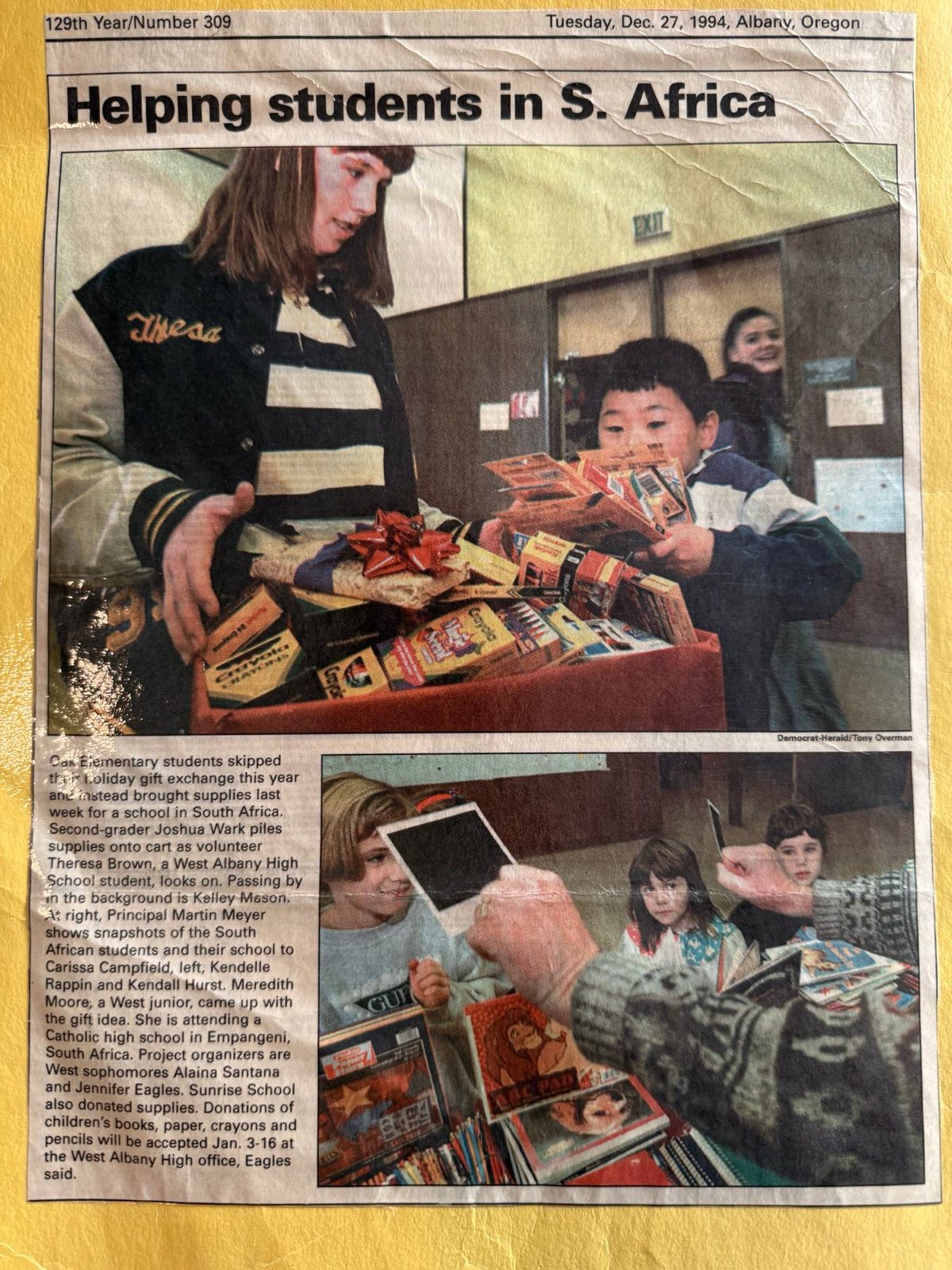Democrat-Herald clipping from December 27, 1994. Headline: Helping students in S. Africa. Second-grader Joshua Wark loads donated school supplies onto a cart.